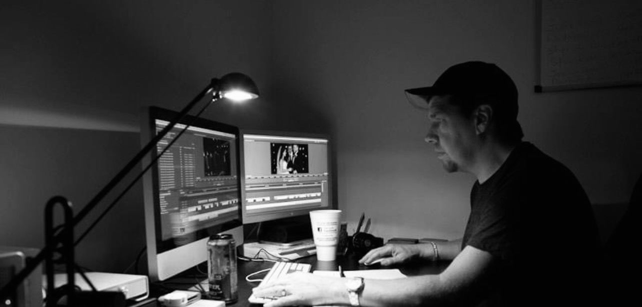 Will Herrington sits at a computer desk editing a wedding film on the screen.