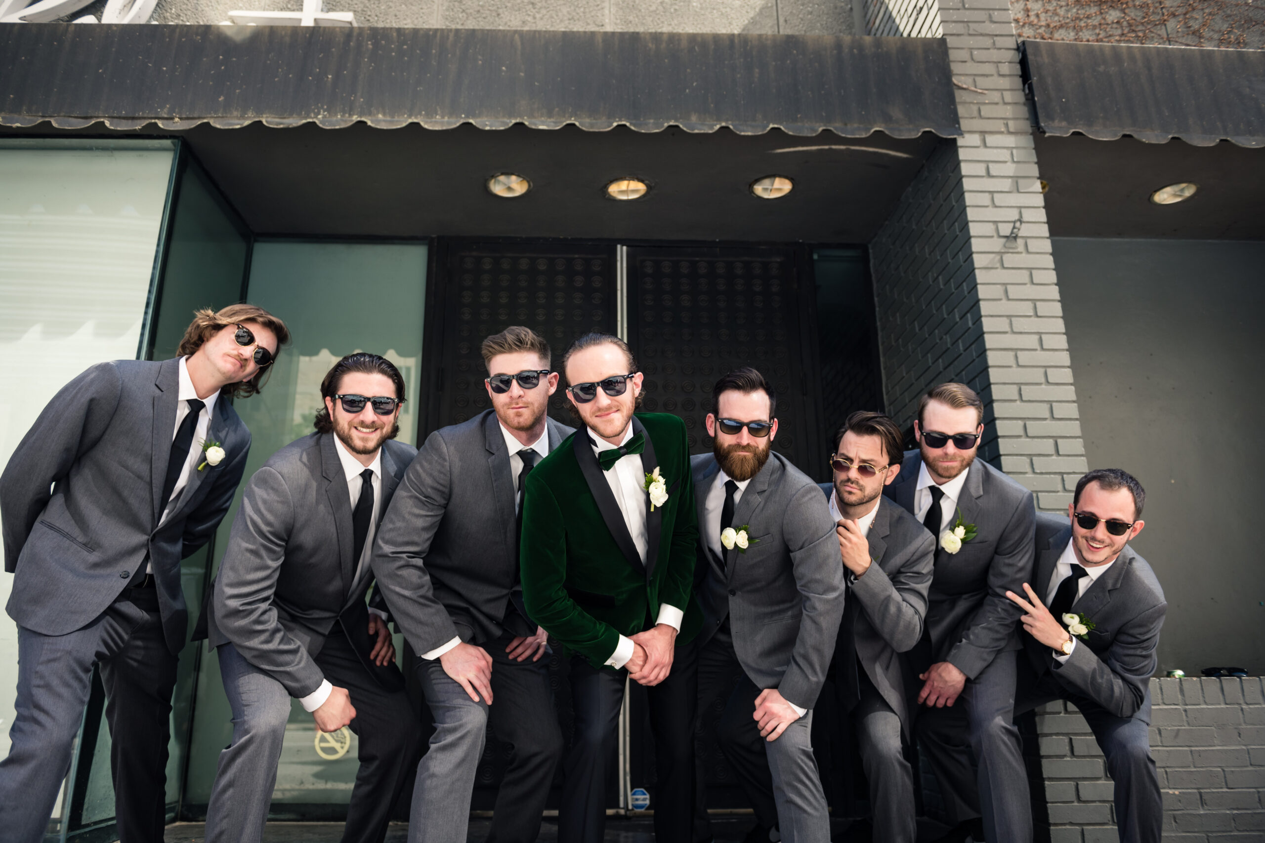 The groom and his groomsmen are bending towards the camera, wearing their black sunglasses.