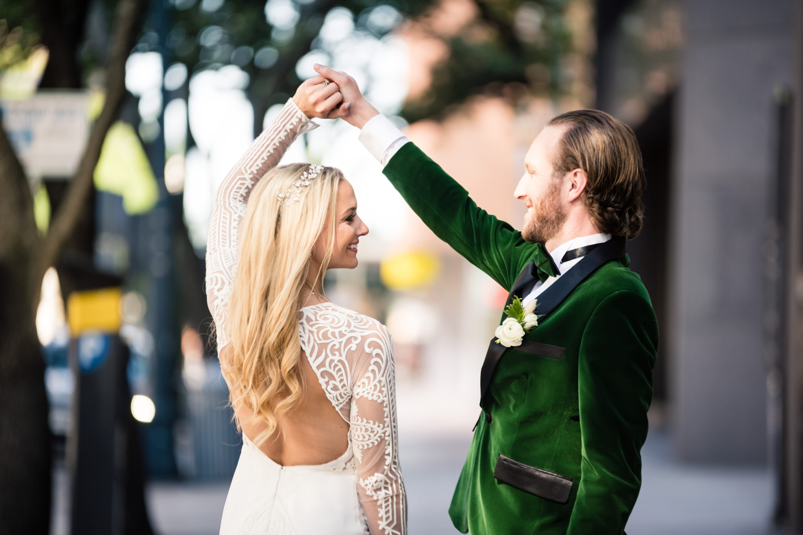 A groom wearing a green velvet suit holds the hand of his bride above her head while he twirls her around on the sidewalk of Downtown Austin, Texas near 800 Congress.
