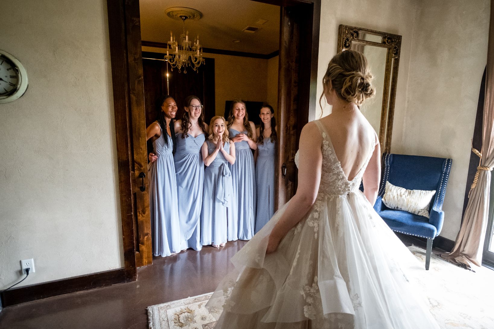 Five bridesmaids in blue long dresses stand in door-away with excitement and joy to see the bride for the first time. 