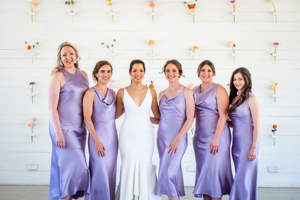 The bride and her bridesmaids in lavender silk are standing in front of The Prospect House's beautiful wall of flowers. 