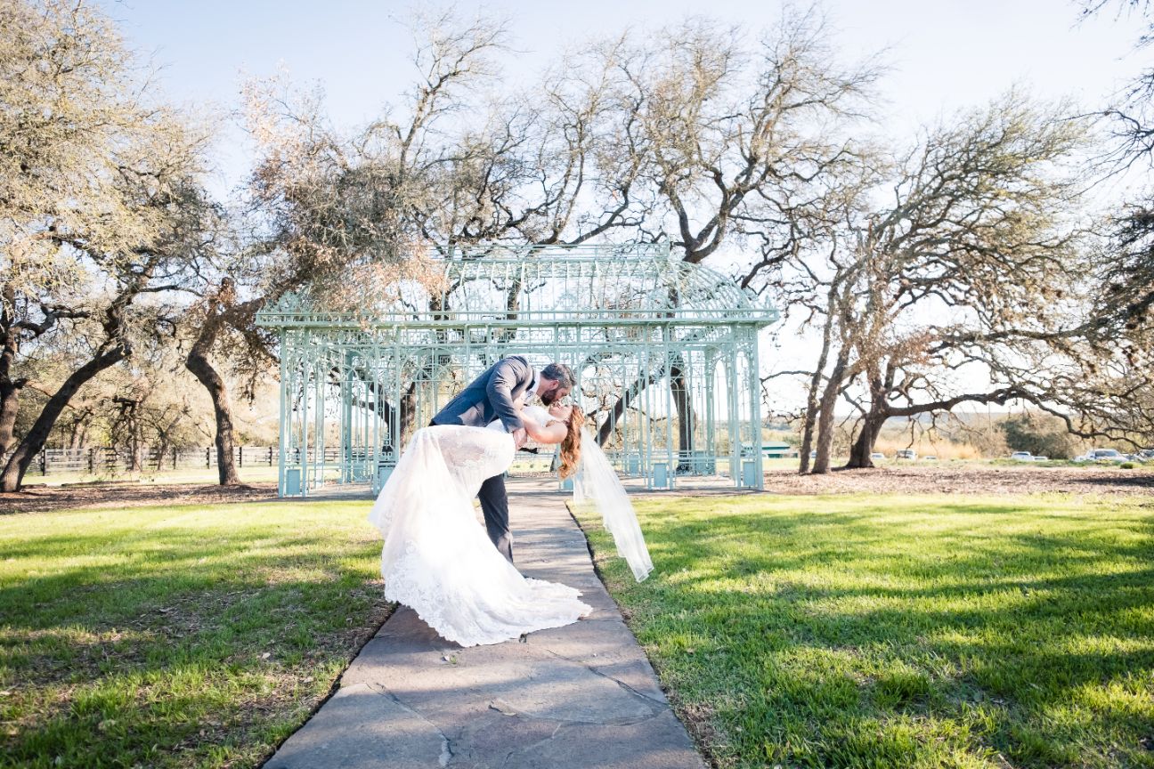 Groom dips bride as they kiss with green gazebo in the background.
