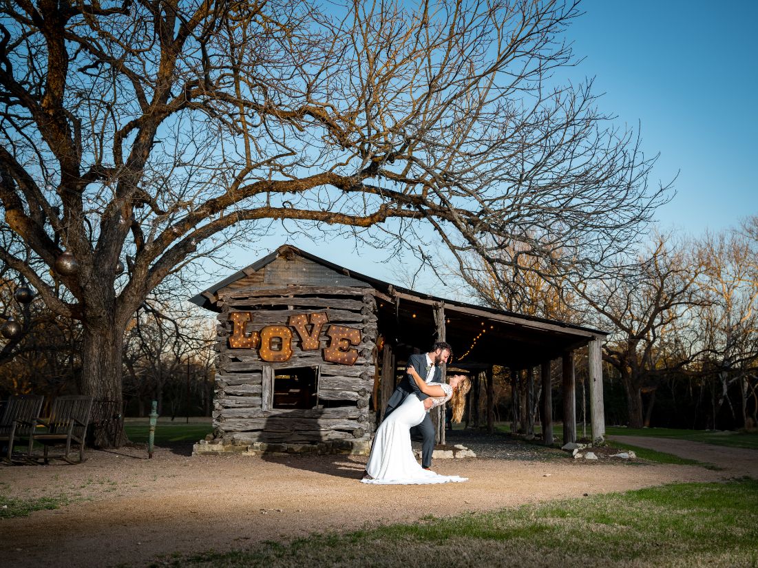 Groom dips bride in front of historic "love shack" cabin at Pecan Springs Ranch wedding venue in Austin, Texas.