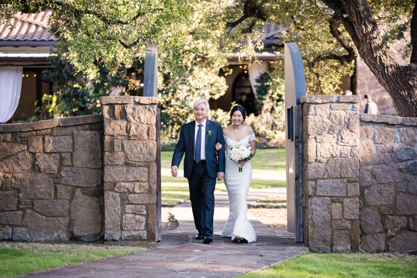 A bride walks with father down the aisle between a stone double door.