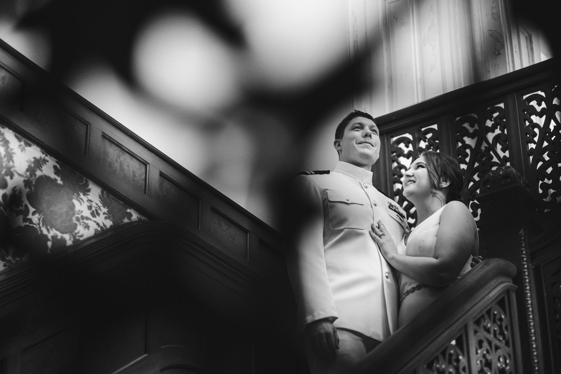 Bride and groom embrace on a wooden staircase with ornate railing.
