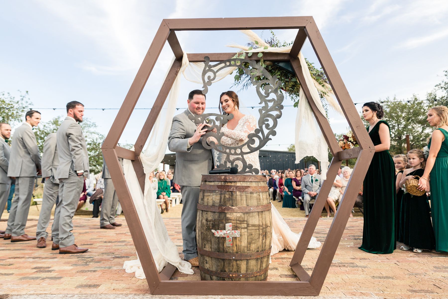 Bride and groom stand near a hexagon shaped wedding altar with wood barrel during wedding at Two Wishes Ranch in Austin Texas.
