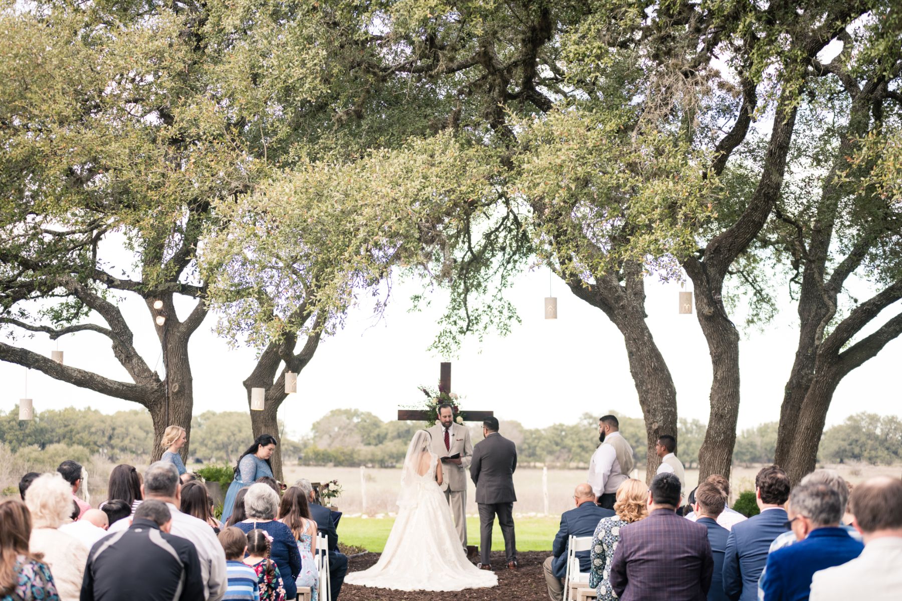 Bride and groom, standing at the altar of their outdoor wedding ceremony at Stonehouse Villa, under large Texas oak trees.