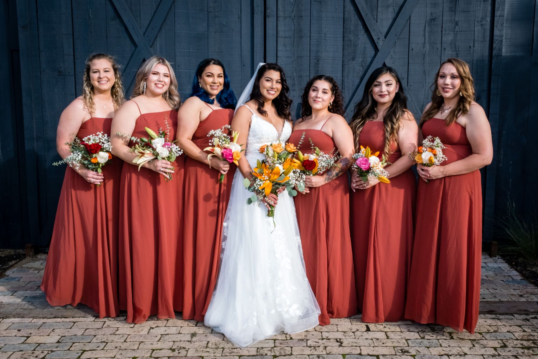 Six bridesmaids wearing oraange dresses stand around bride and pose for photo during wedding at Two Wishes Ranch in Austin Texas.