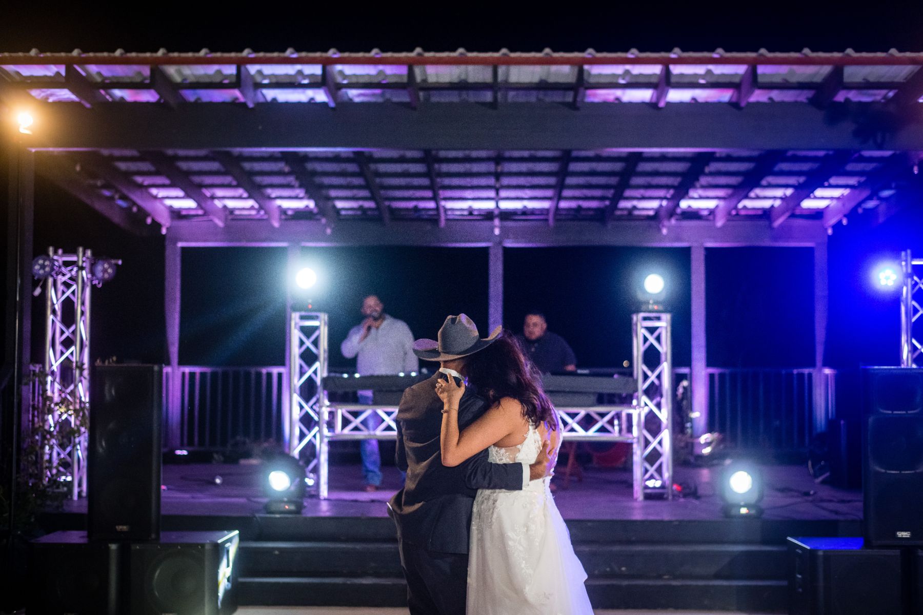Bride and groom hug each other and watch the stage in front of them at the Two Wishes Ranch pavillion. 