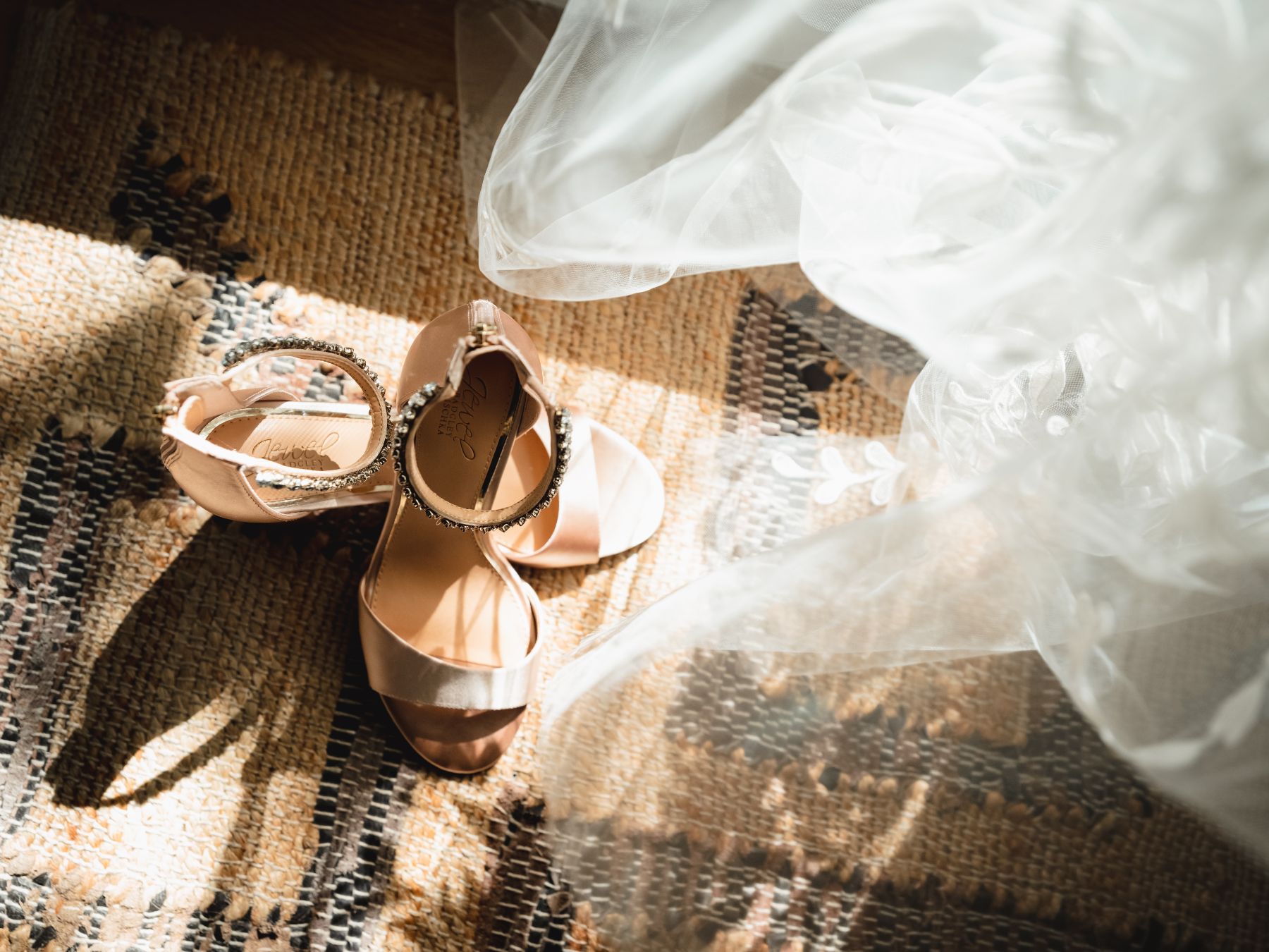 Shoes laid out with a wedding veil, a top of a rustic rug.