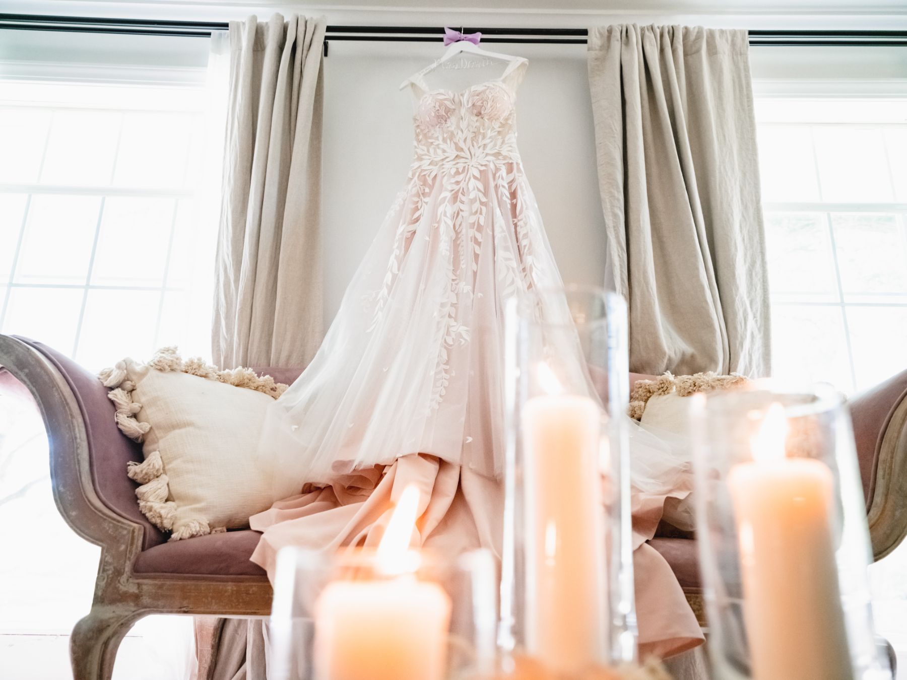 A wedding dress hangs a top, a vintage blush couch with lit candles in the foreground at the bridal suite of the Addison Grove in Austin, Texas.