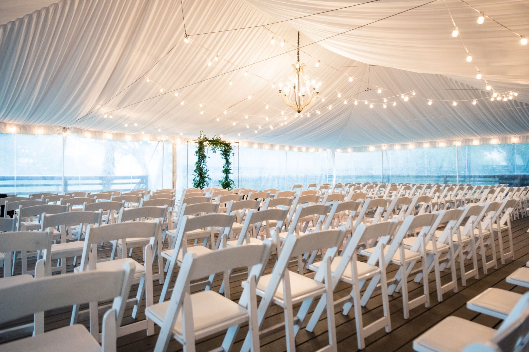 Wedding ceremony set up under an elegant white tent with bistro lighting and chandeliers at Stonehouse Villa.