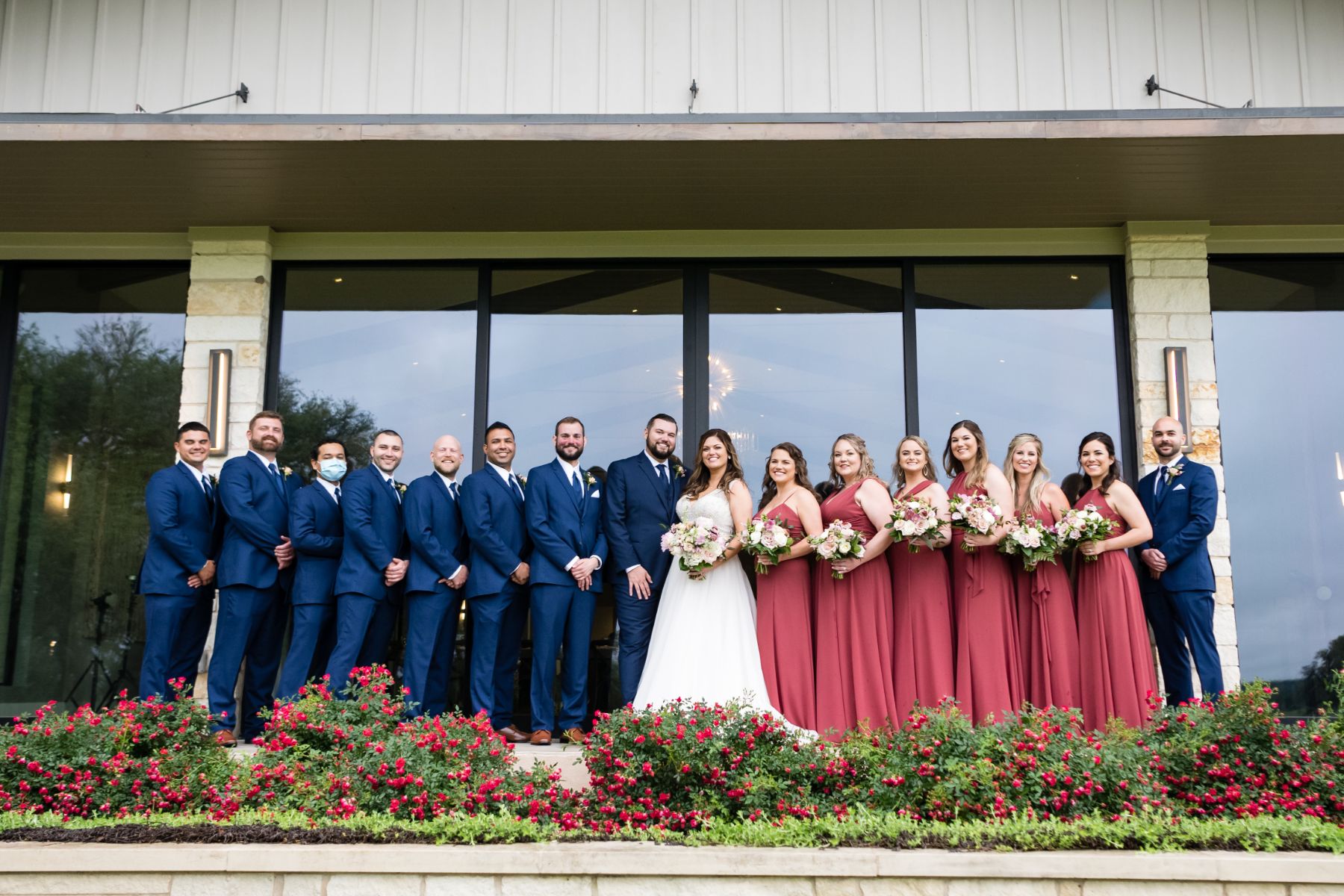 Bride and groom with their bridal party are lined up in front of a limestone building with large windows at Stonehouse Villa.