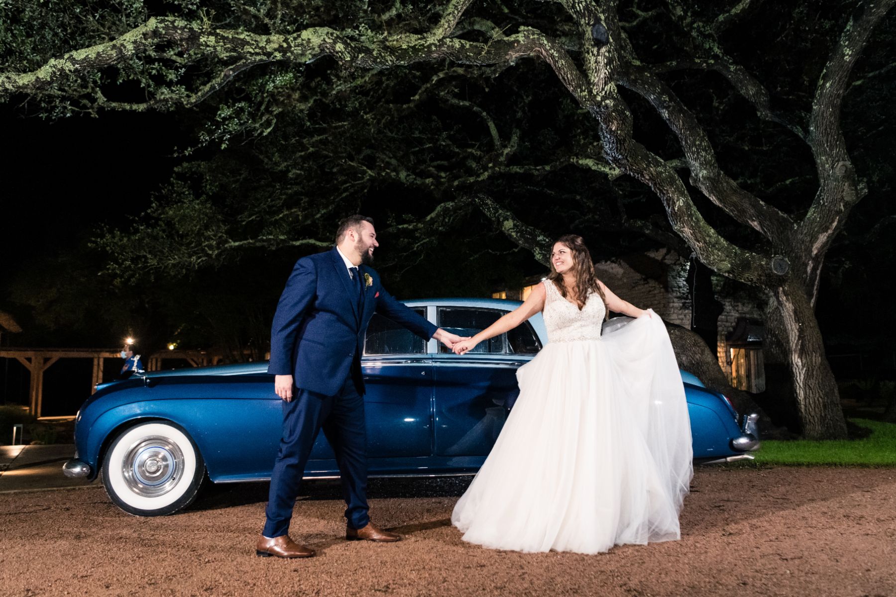 Bride and groom, hold hands in front of a luxury blue car.