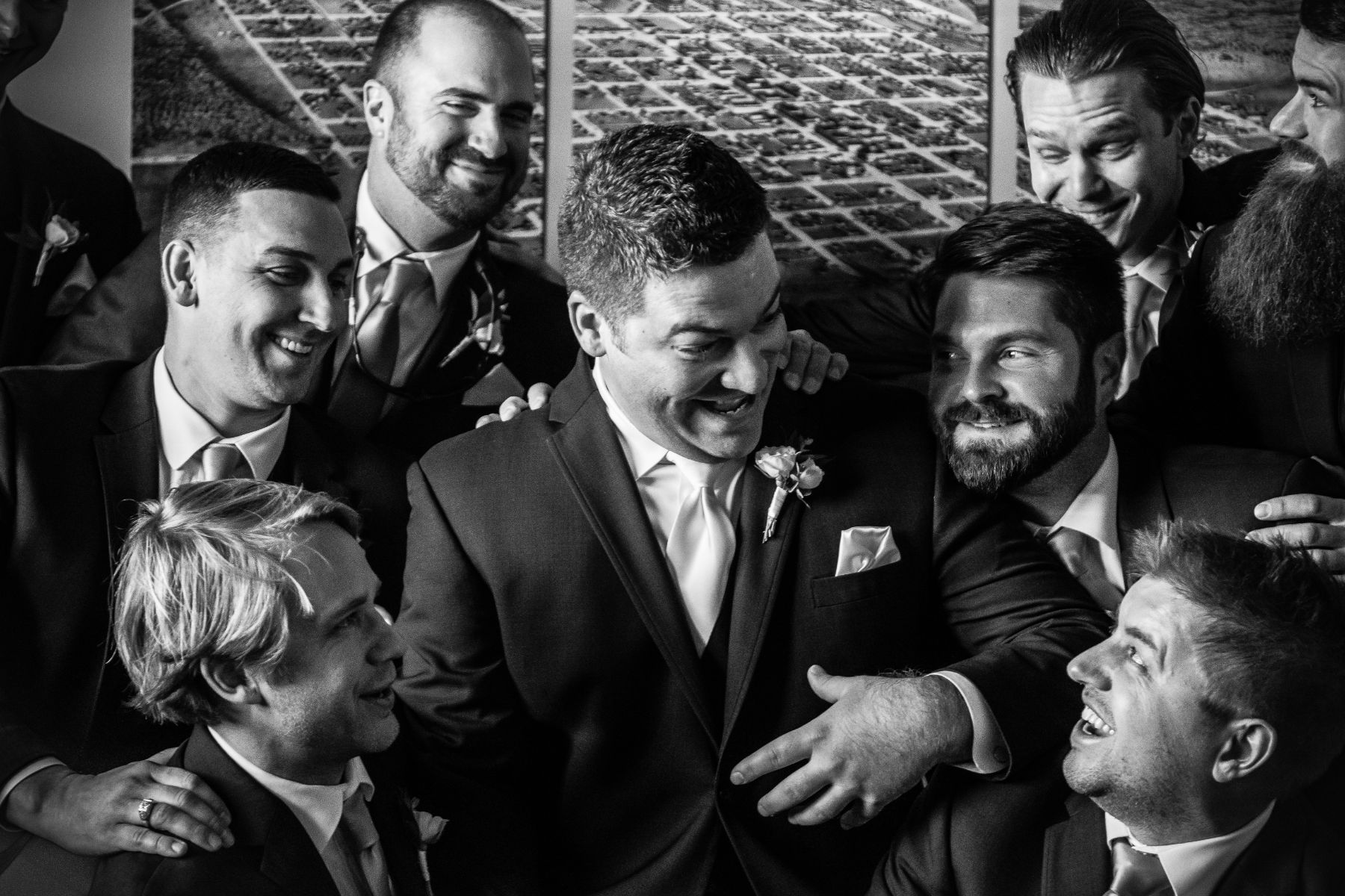 A groom is surrounded by his groomsmen, who are cheering and smiling at him.