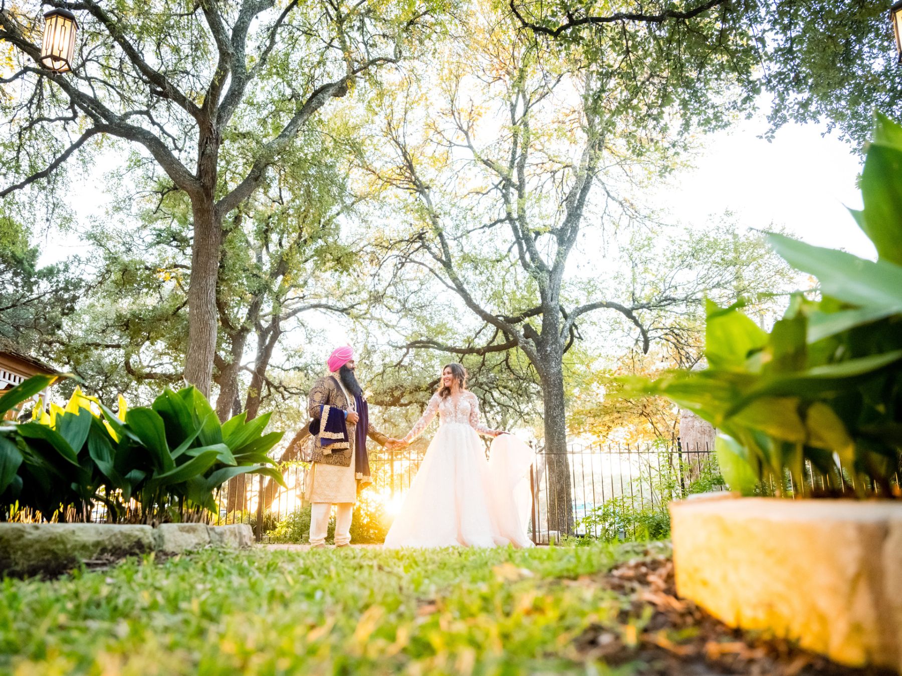 Bride and groom hold hands outdoors in a garden space with sun rays illuminating the couple.